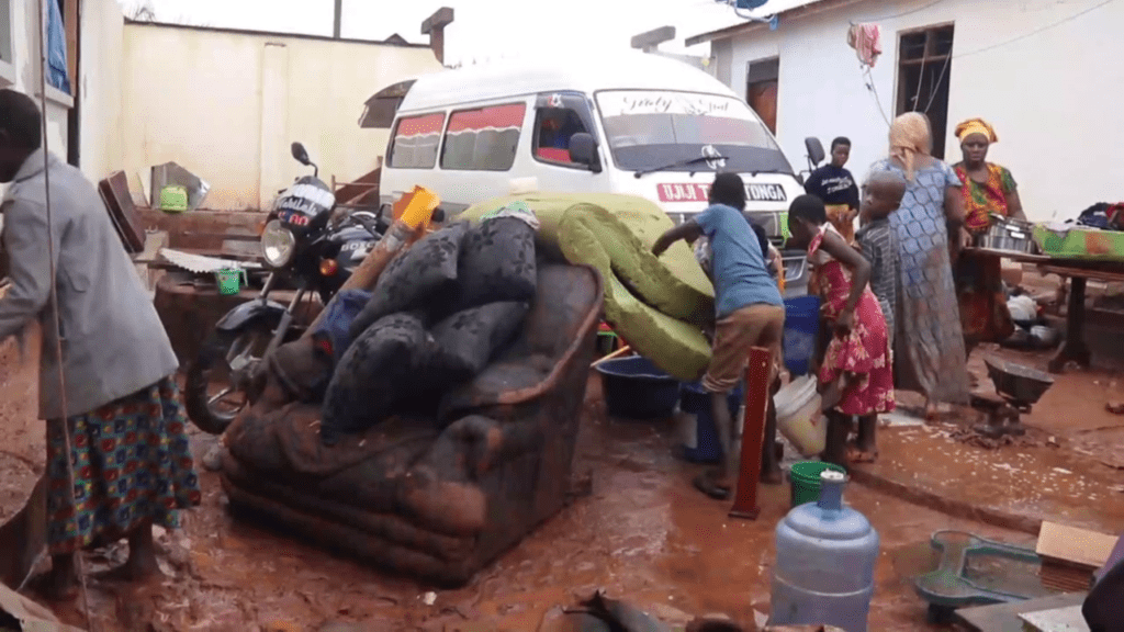 Soaked mattresses and belongings sit in the mud of Upendo Mlary's home in Burega, Kigoma, after floodwaters—exacerbated by blocked drainage—caused her bedroom wall to collapse on December 10, 2025.